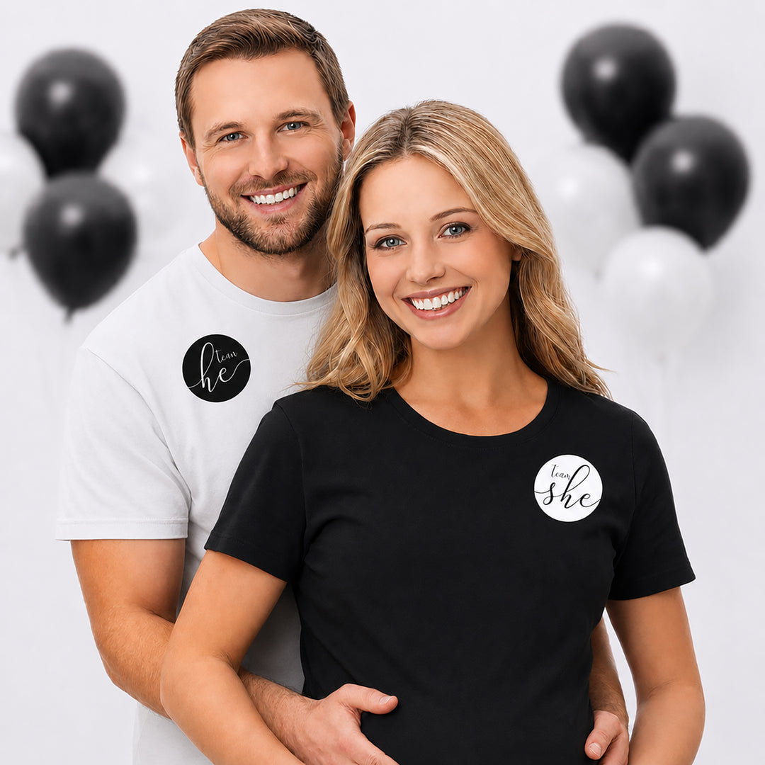 A smiling couple poses together wearing black and white team he and team she stickers
